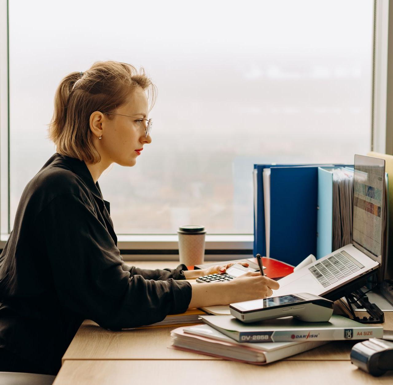 Dedicated woman using laptop and calculator in modern office setting.