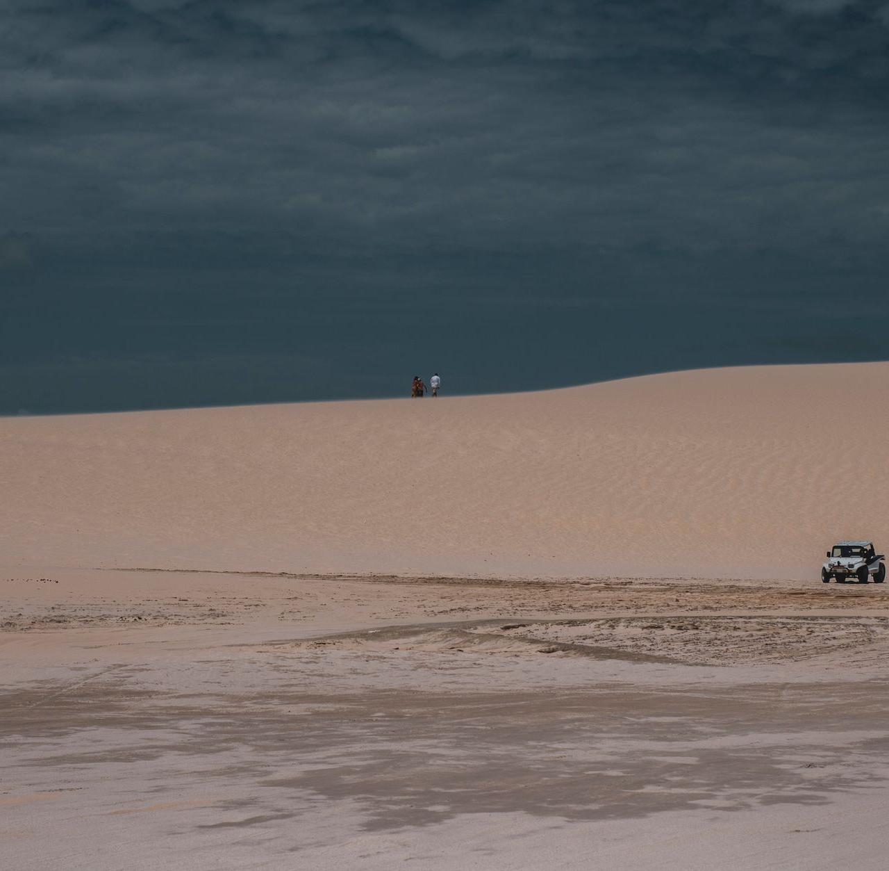 Jeep navigating the sandy dunes of Jericoacoara desert under a cloudy sky.