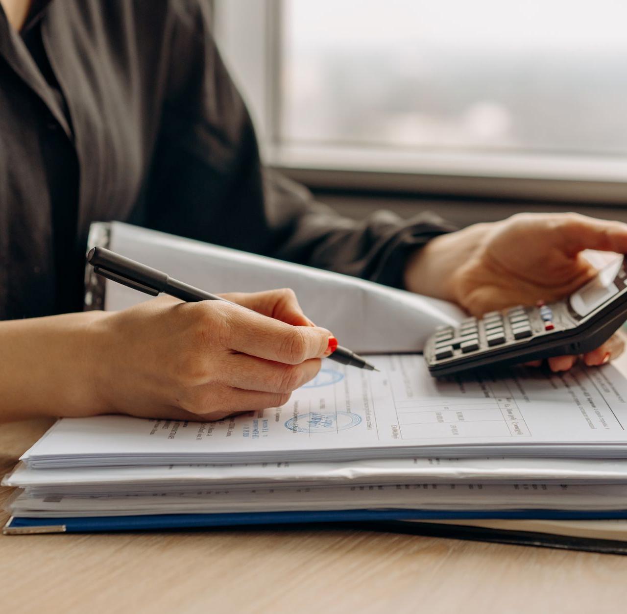 Close-up of person using a calculator with financial documents in an office.