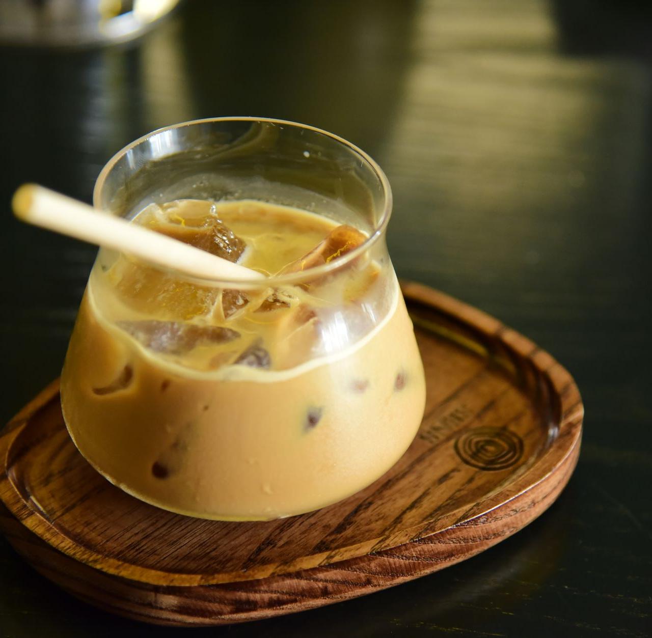 Delicious iced coffee served in a glass with a bamboo straw on a wooden tray, perfect for a refreshing drink.