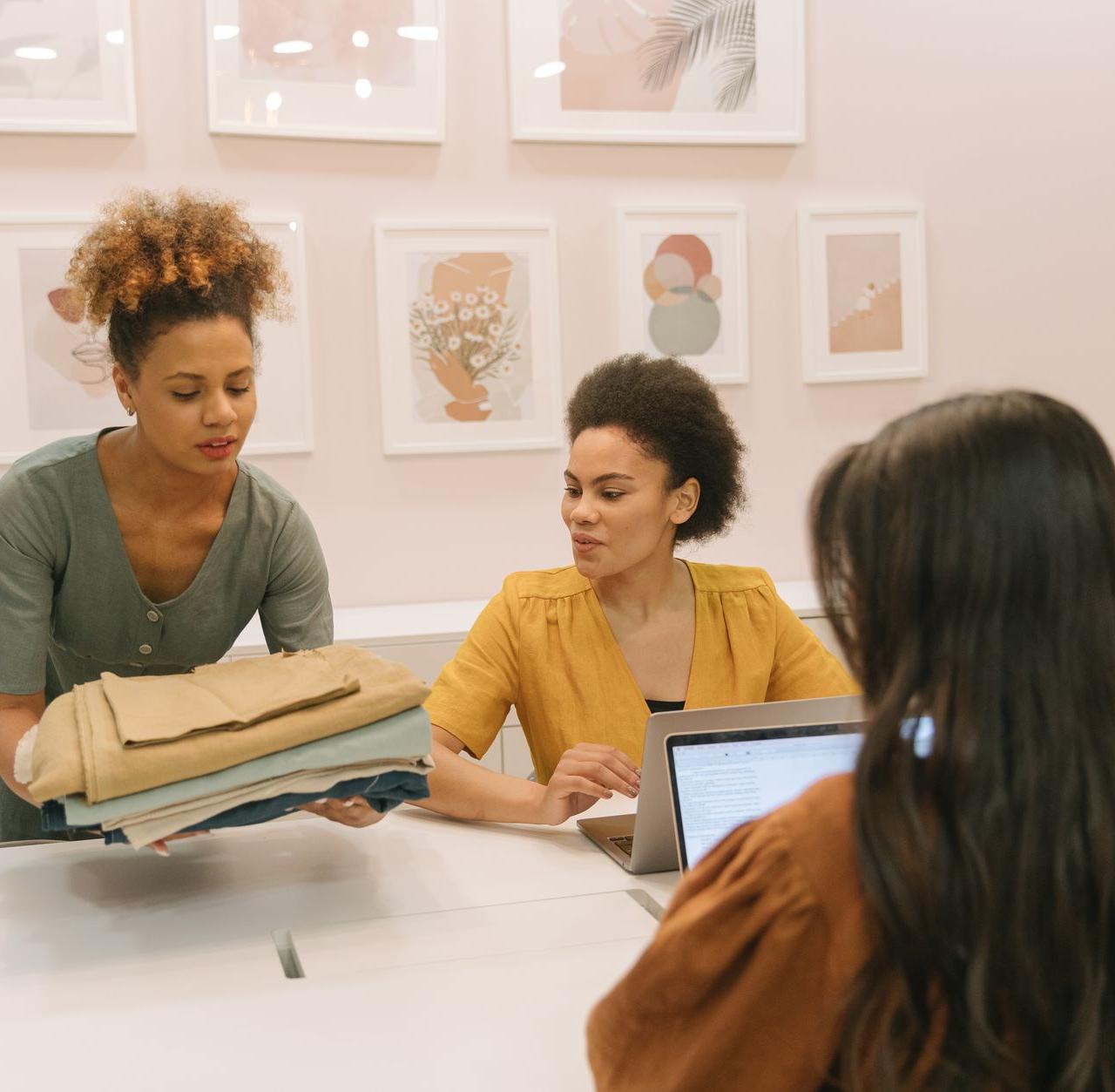 Three women working together in a modern boutique, discussing fashion and business strategies.