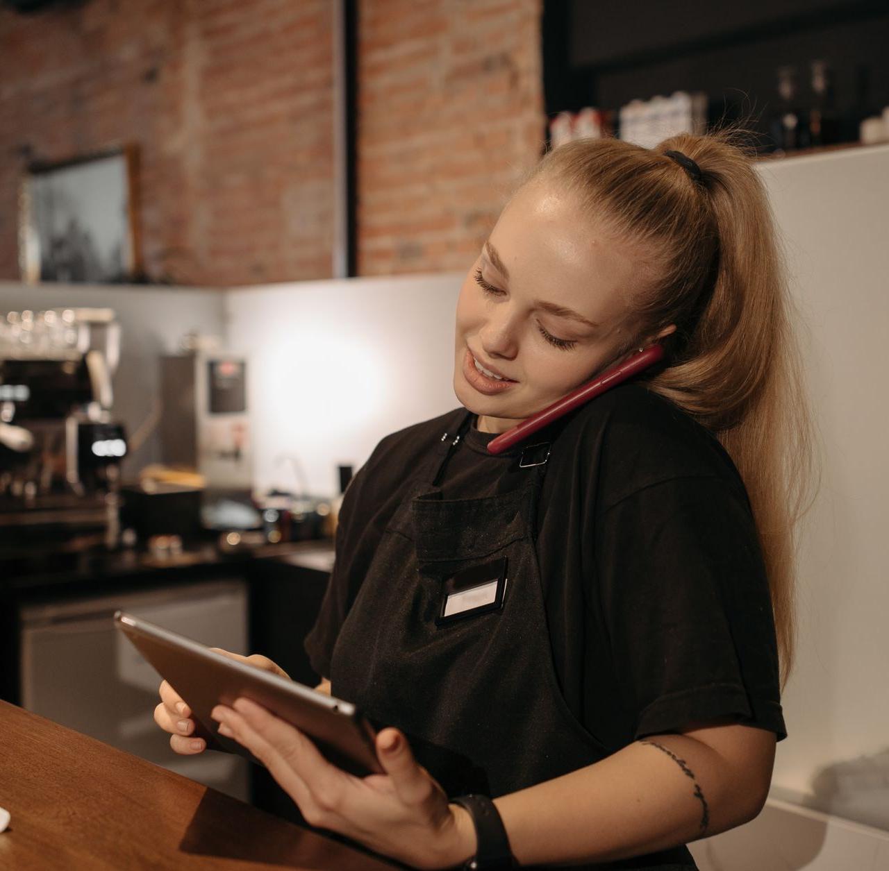 Young woman in café multitasks with a tablet and phone at the counter.