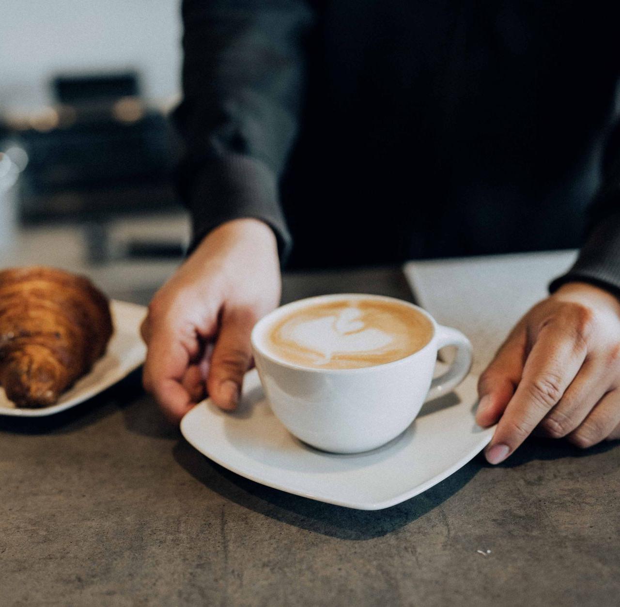 A barista places a latte and croissant on a counter, creating a warm cafe atmosphere.