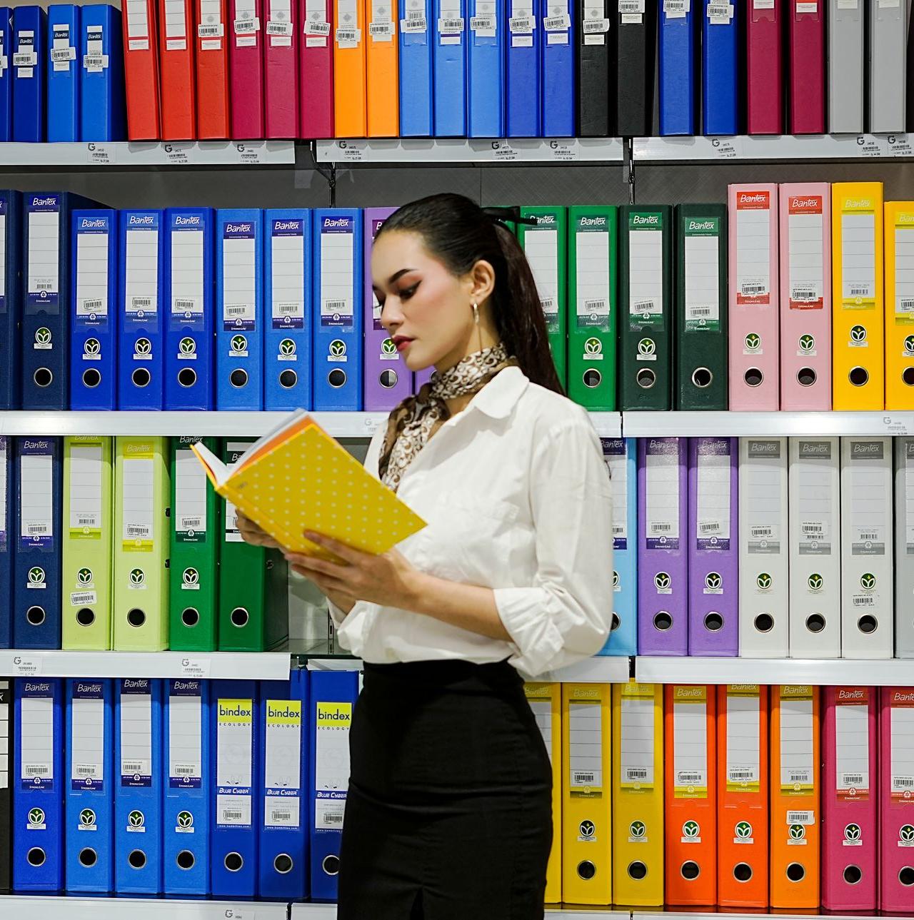 A young woman reads a file in front of a vibrant array of office binders.