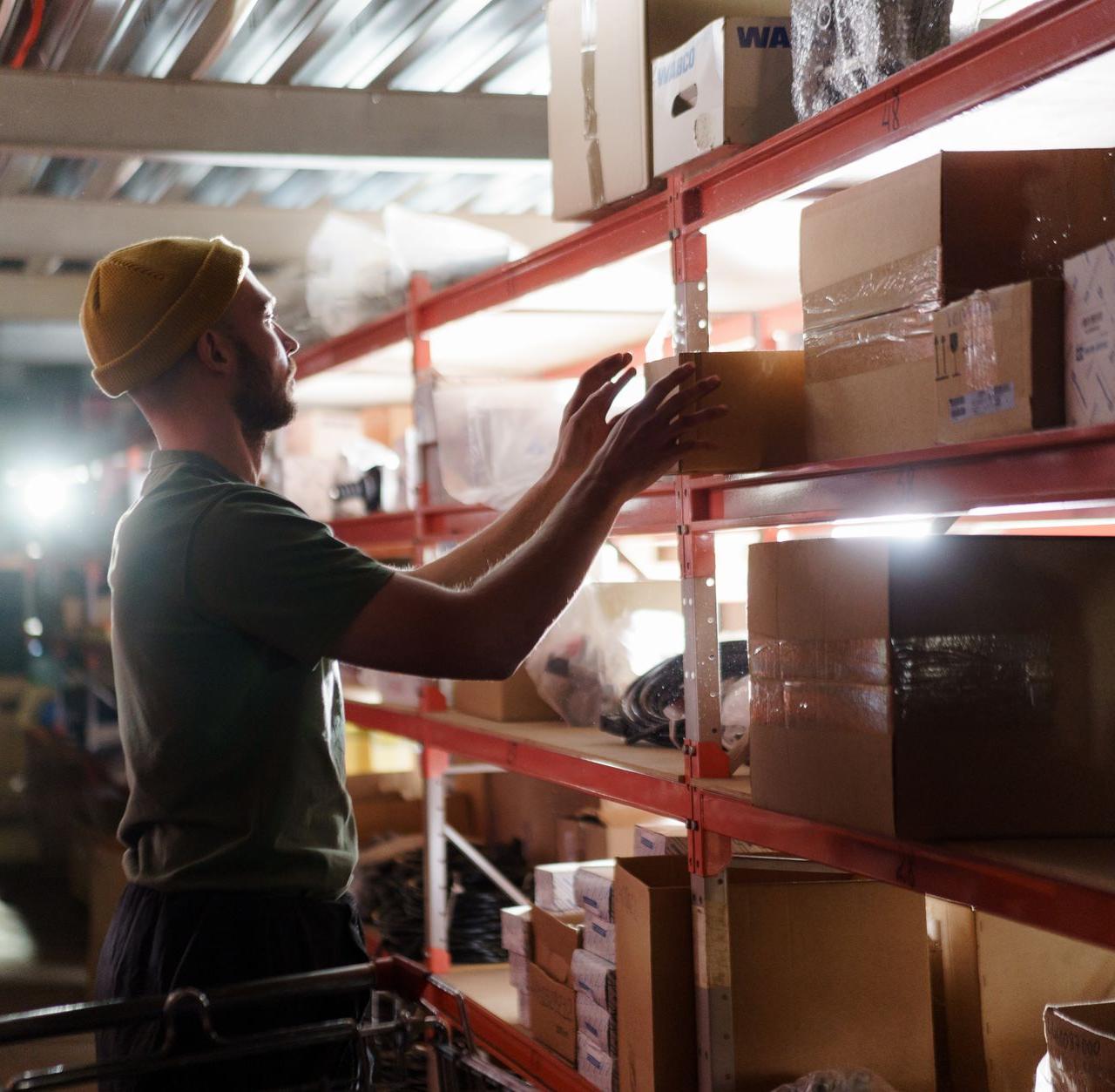 Worker organizing boxes on shelves in a warehouse, focused on logistics and storage management.