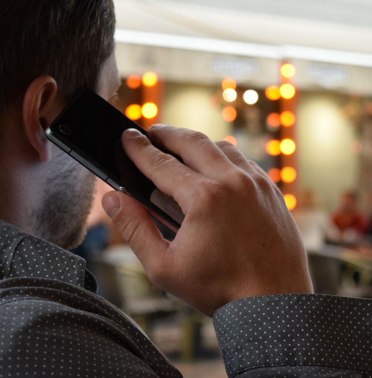 Close-up of a businessman in a dotted shirt making a call in a lively indoor setting with warm lights.