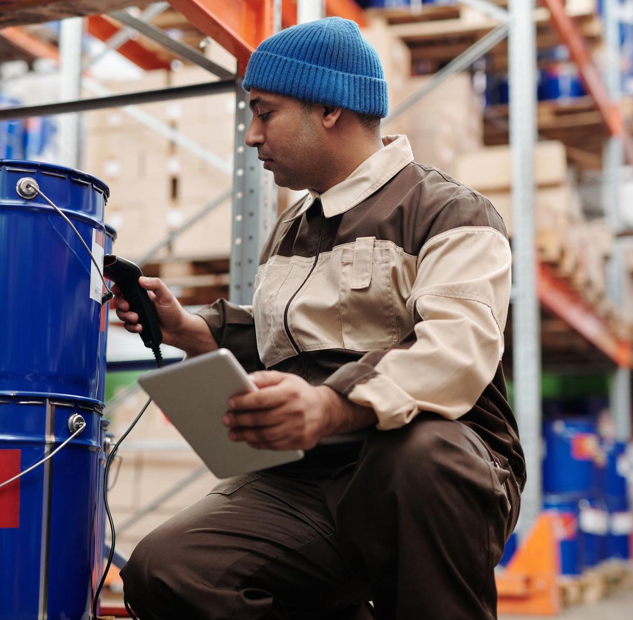 Warehouse employee scanning inventory using tablet and scanner in industrial storage area.