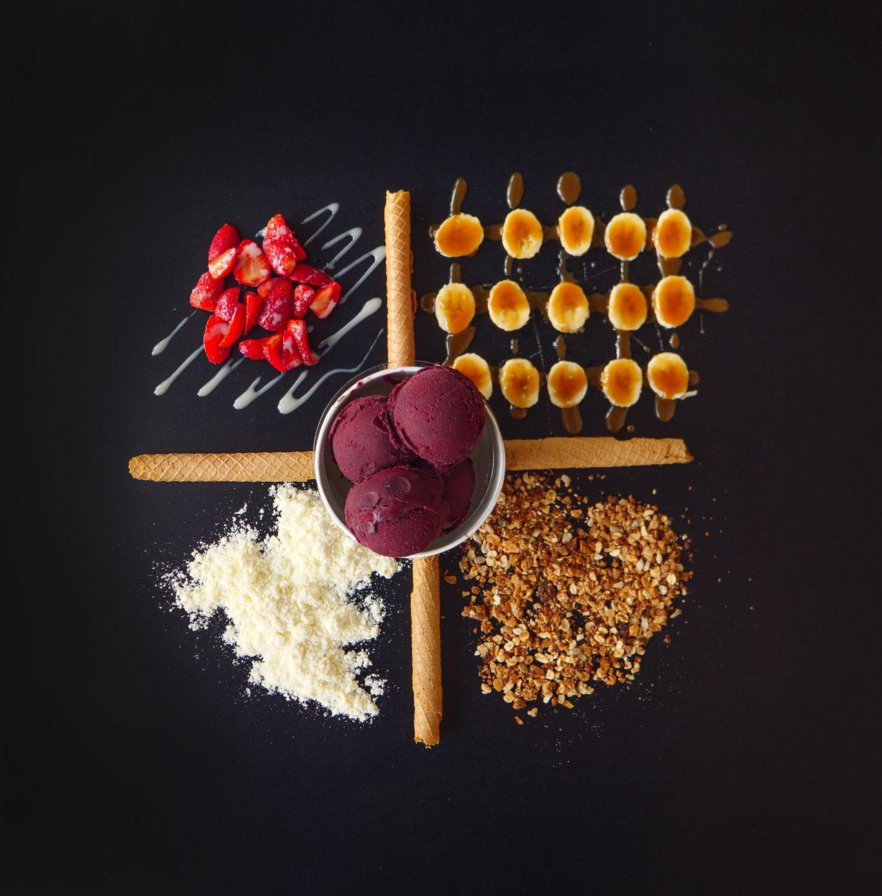 Flat lay of ice cream with strawberries, nuts, and wafers on a black background.