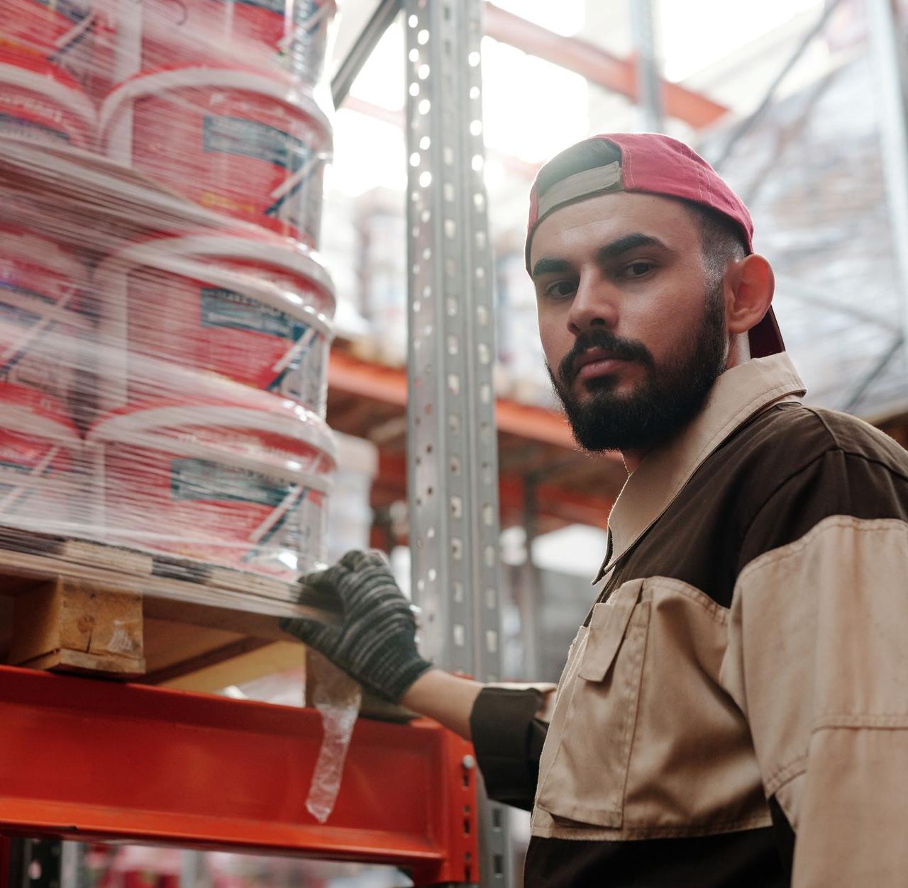 Portrait of a male warehouse worker standing next to stacked paint buckets indoors.