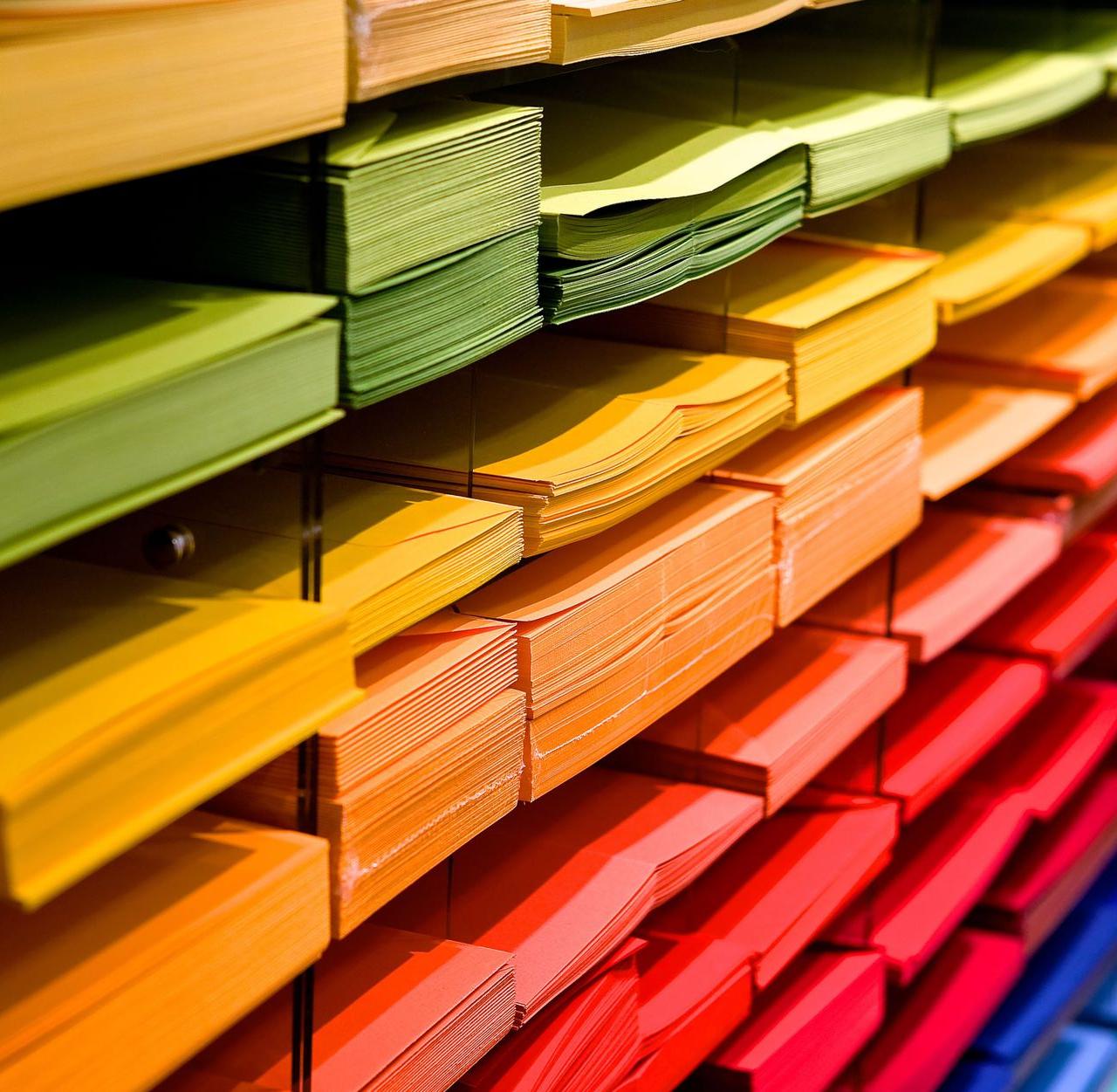 Vibrant multicolored paper stacks arranged on shelves in a stationery store.
