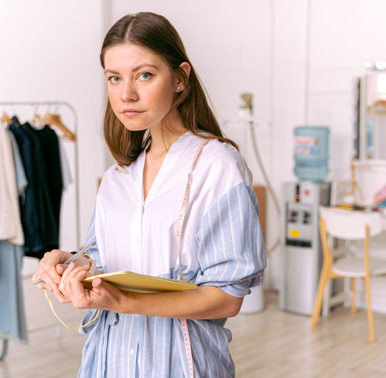 Fashion designer in studio holding notebook, pondering clothing designs.