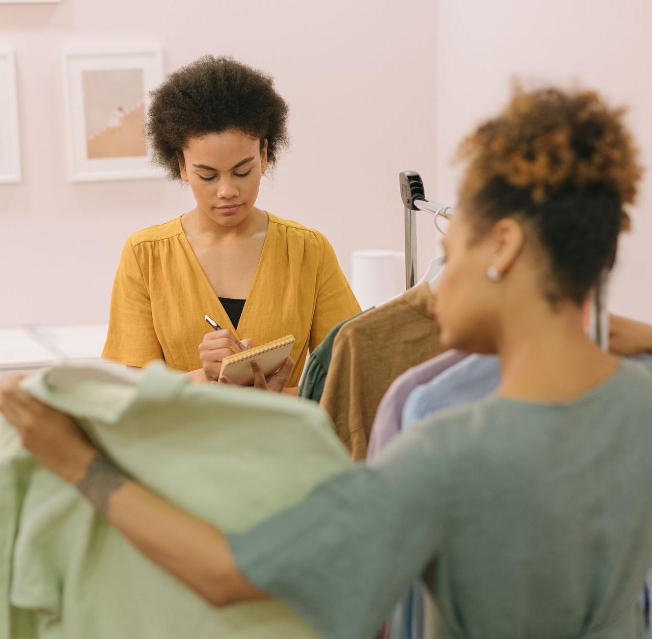 Two women collaborating on a new fashion collection, taking notes and examining garments.