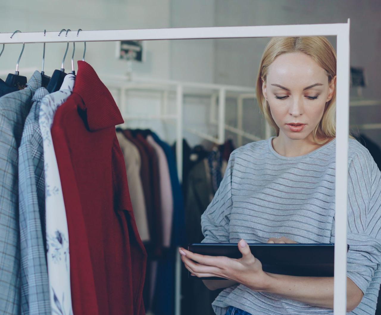 Female retail employee using a tablet for inventory management in a clothing store.