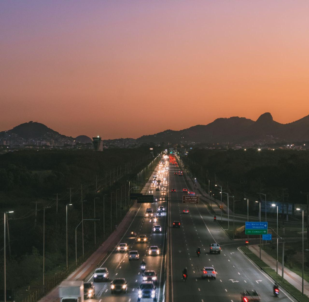 Captured aerial view of a busy highway with city skyline and mountains at sunset.