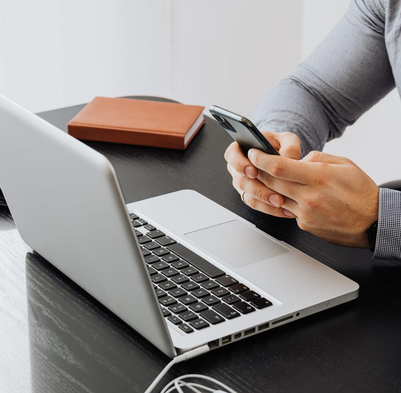 An adult using a smartphone at an office desk with a laptop for work.