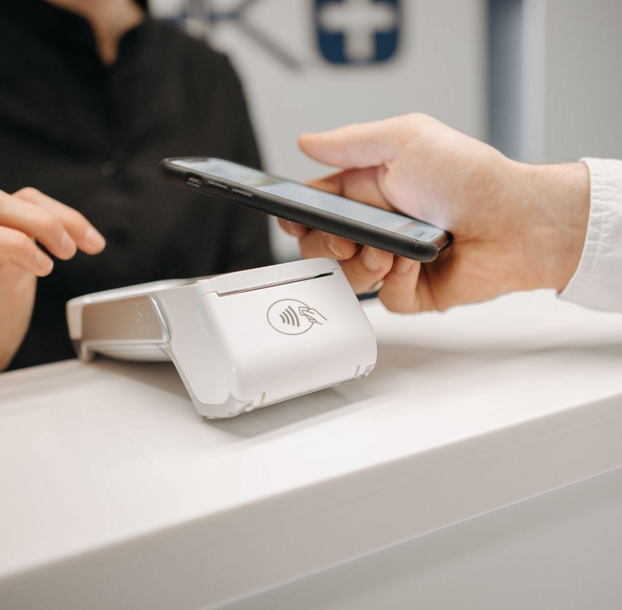 Person using a smartphone for contactless payment at a retail counter, highlighting cashless convenience.