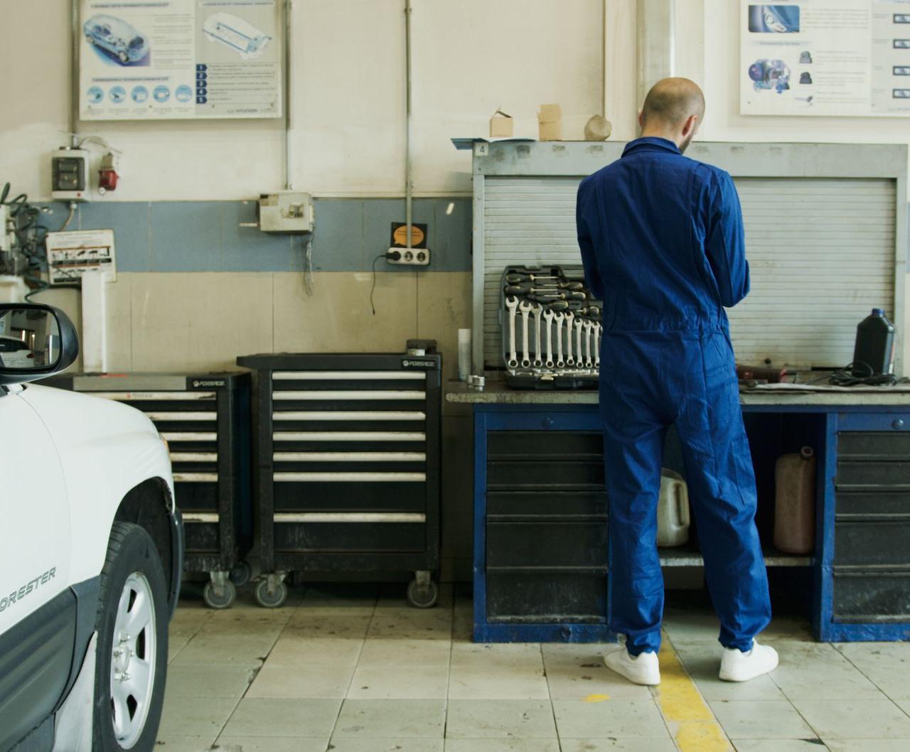 Mechanic in blue overalls inspecting a white car in a well-equipped garage.