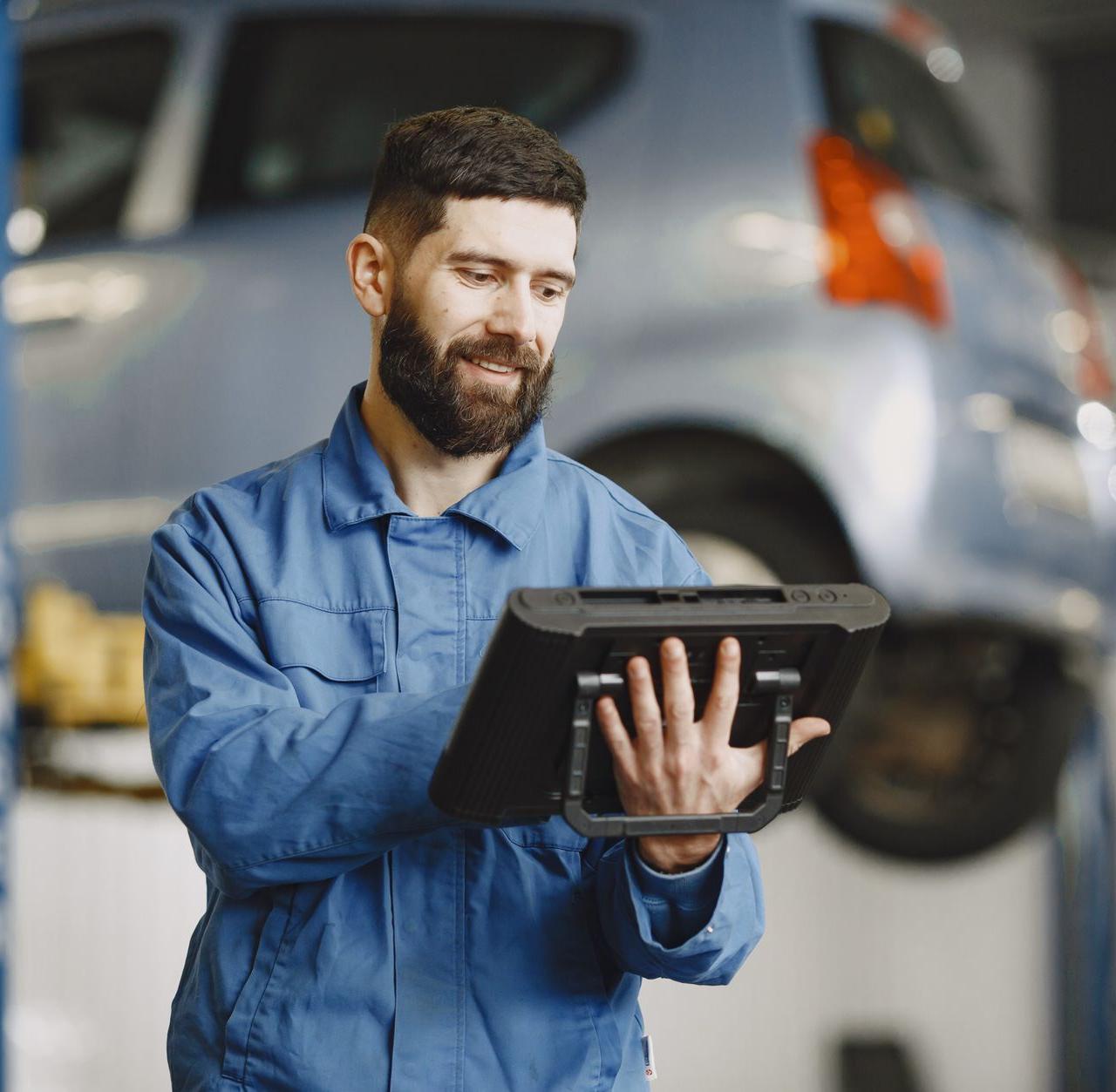 Smiling auto mechanic uses digital tablet in car repair shop environment.