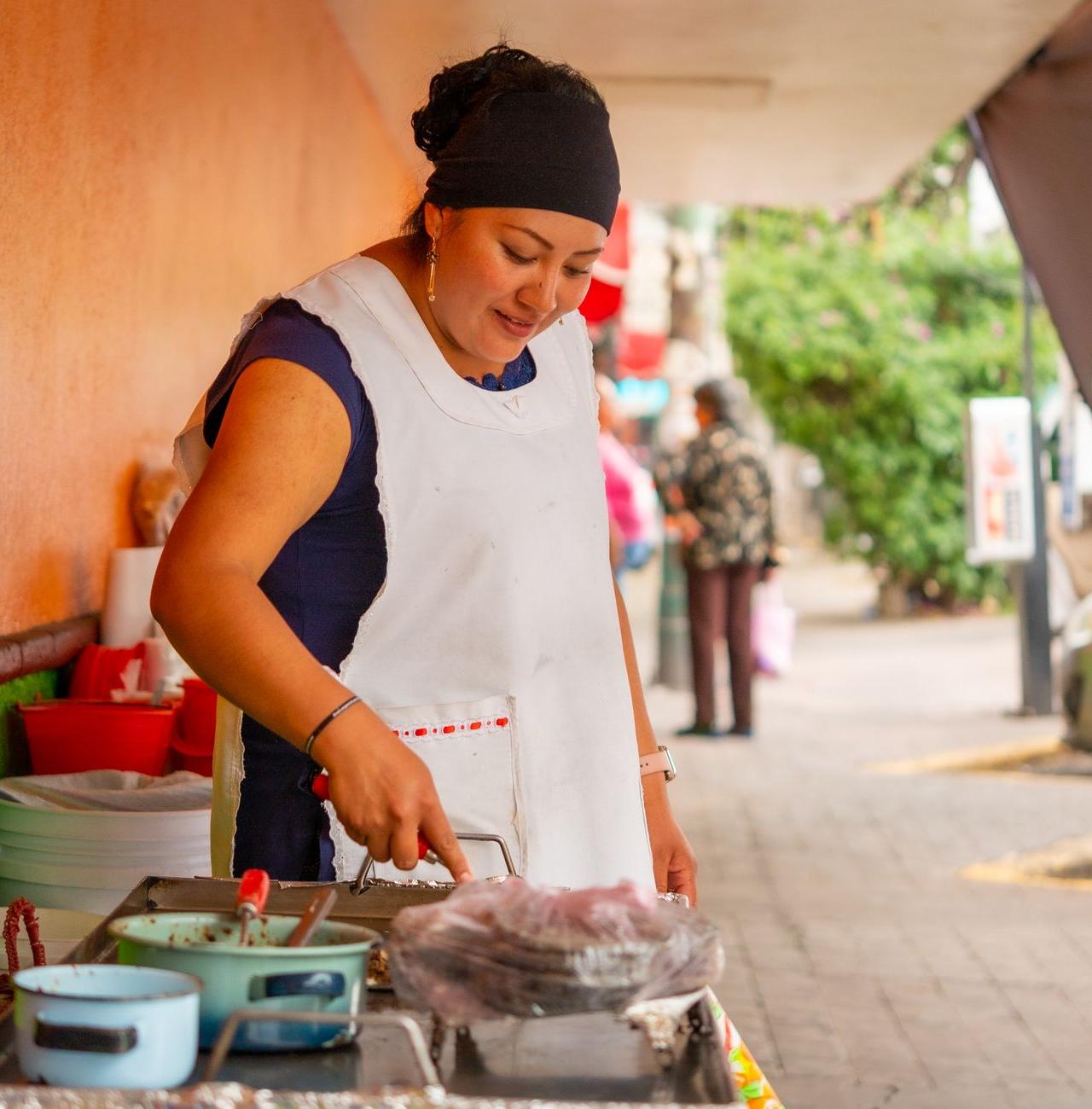 A woman preparing street food at an outdoor market in Ciudad de México. Captured in a vibrant urban setting.