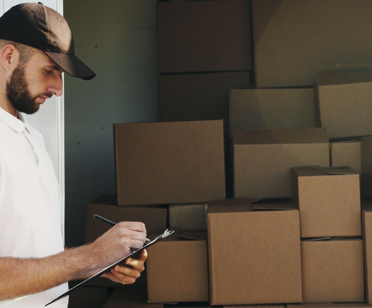 Deliveryman writing on clipboard next to stacked cardboard boxes in a van.