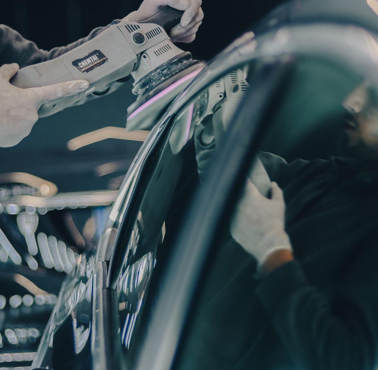 Close-up of car detailing process with polishing machine and reflective surface in workshop.