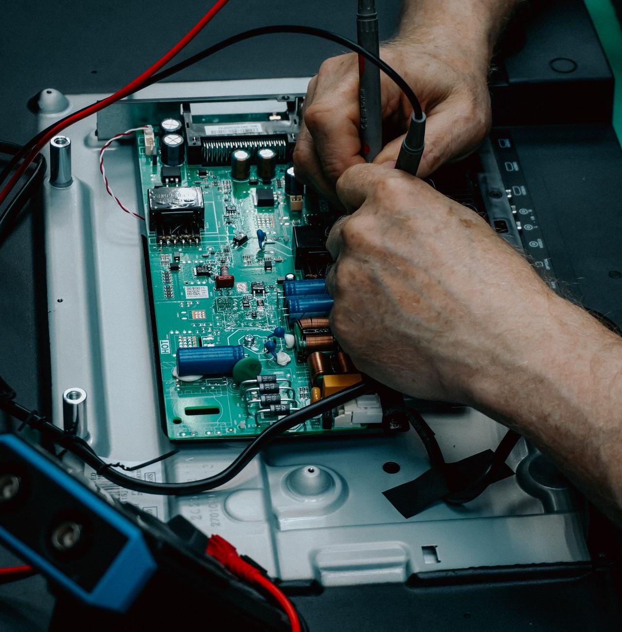 Close-up of hands repairing electronic circuit board, showcasing detailed technology work.
