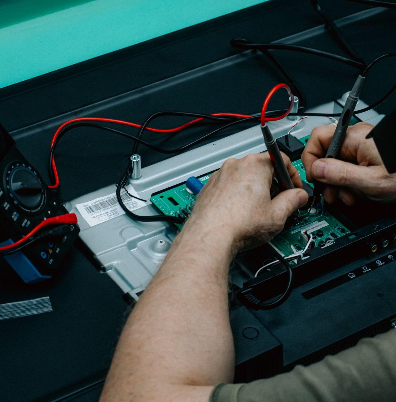A technician uses a multimeter to repair a circuit board, focusing on precision electronics work.