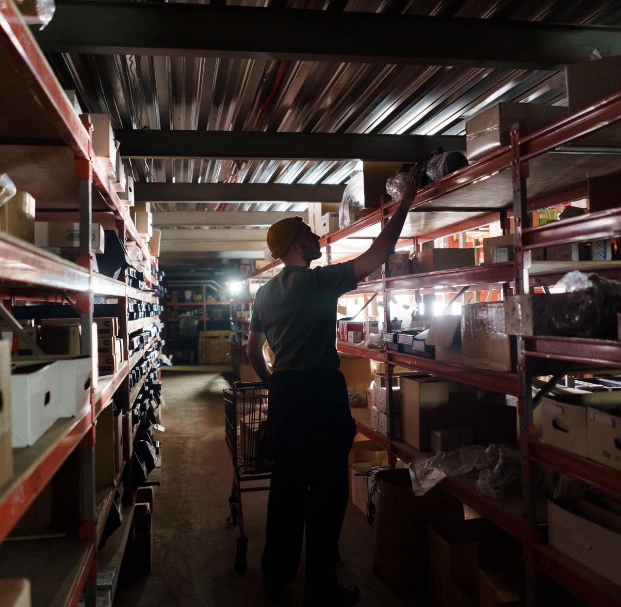 A worker arranging inventory on shelves in a dimly lit warehouse, utilizing efficient storage practices.