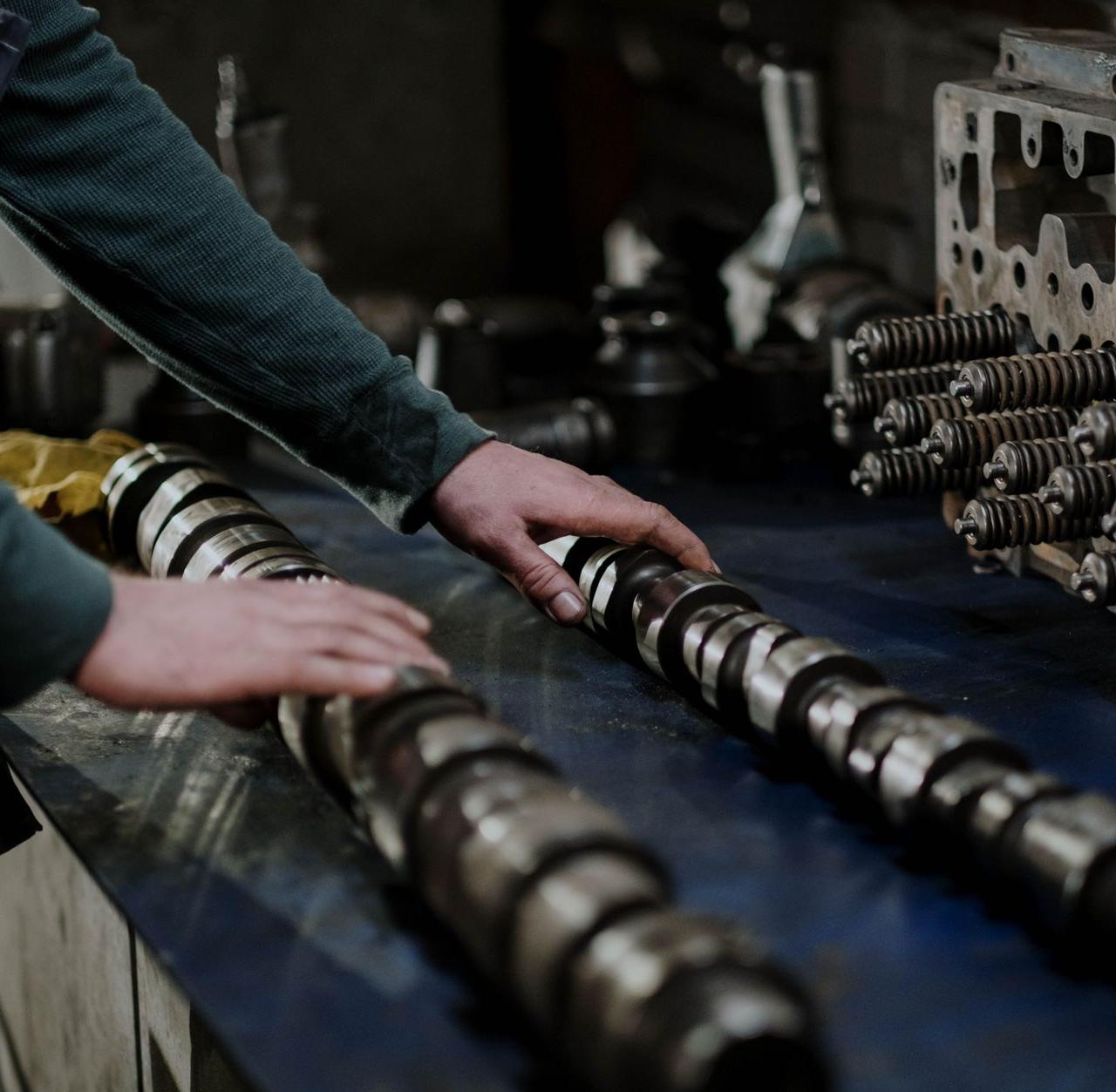 Worker handling camshafts and cylinder head in a mechanic workshop.
