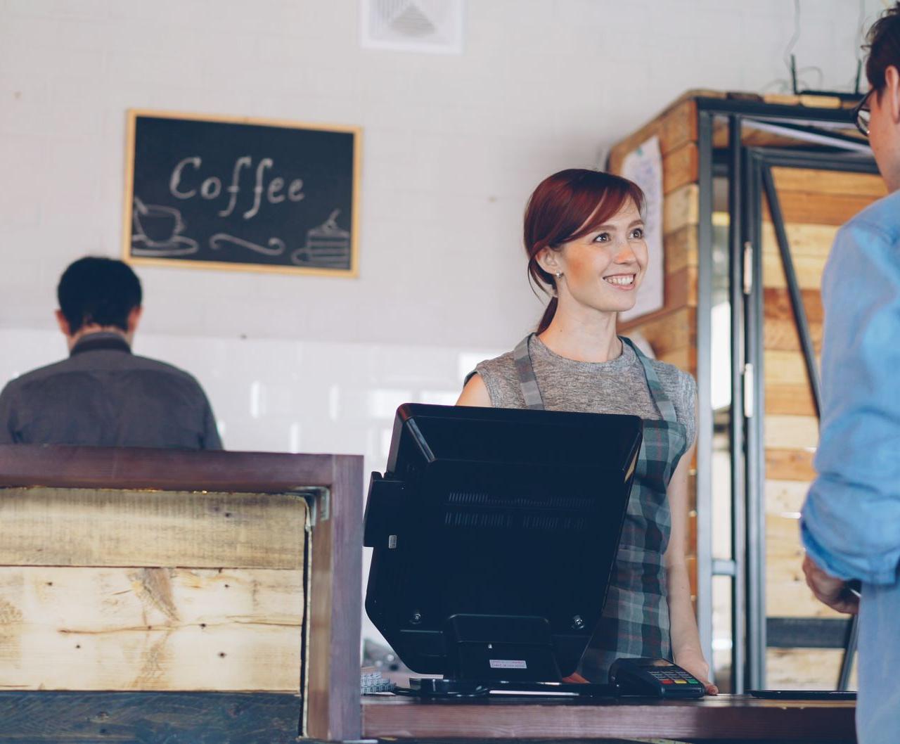 A smiling barista assists a customer at a coffee shop counter, creating a warm atmosphere.