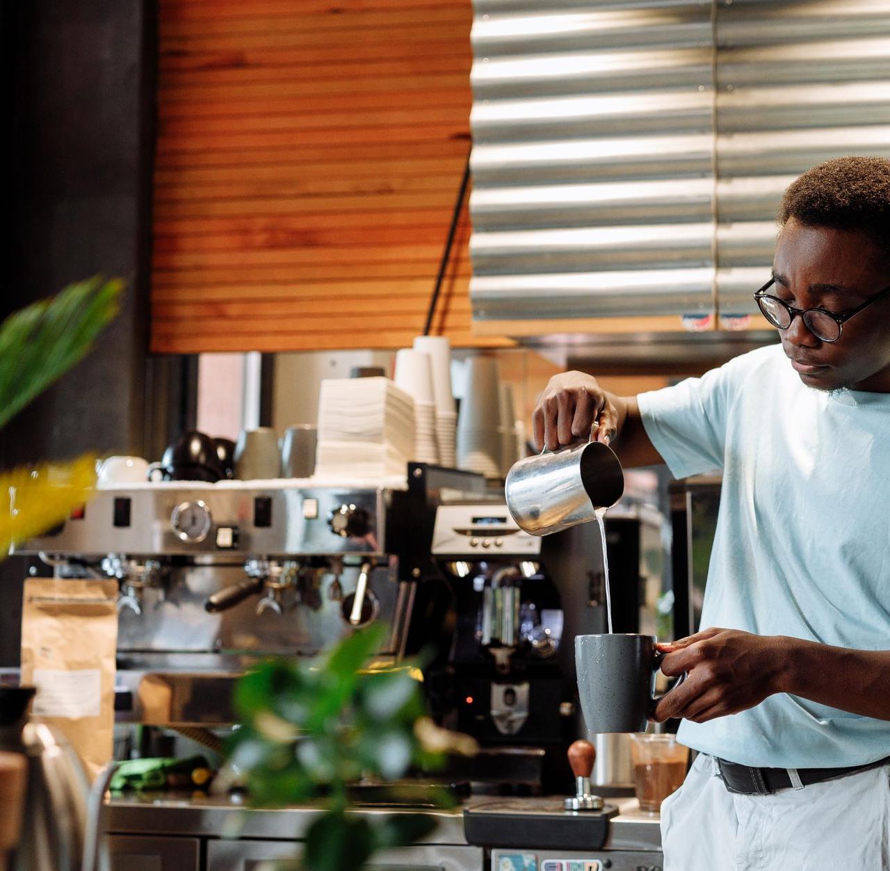 Barista pours steamed milk into coffee mug at a trendy cafe.