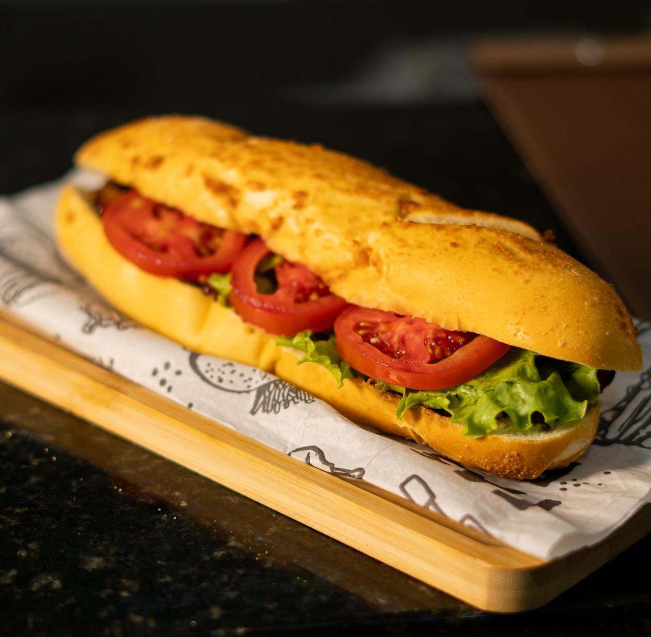 Tasty sandwich with fresh tomato slices and lettuce on a wooden board, perfect for a quick meal.
