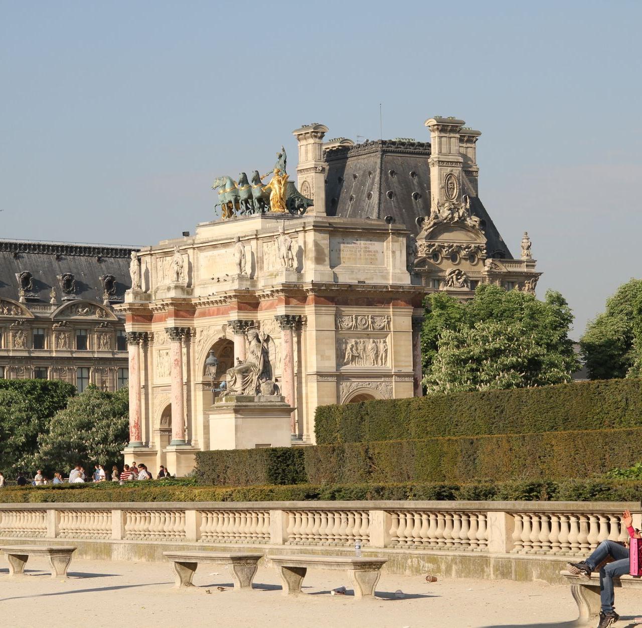 Sunny day at the Arc de Triomphe du Carrousel in Paris with people relaxing nearby.