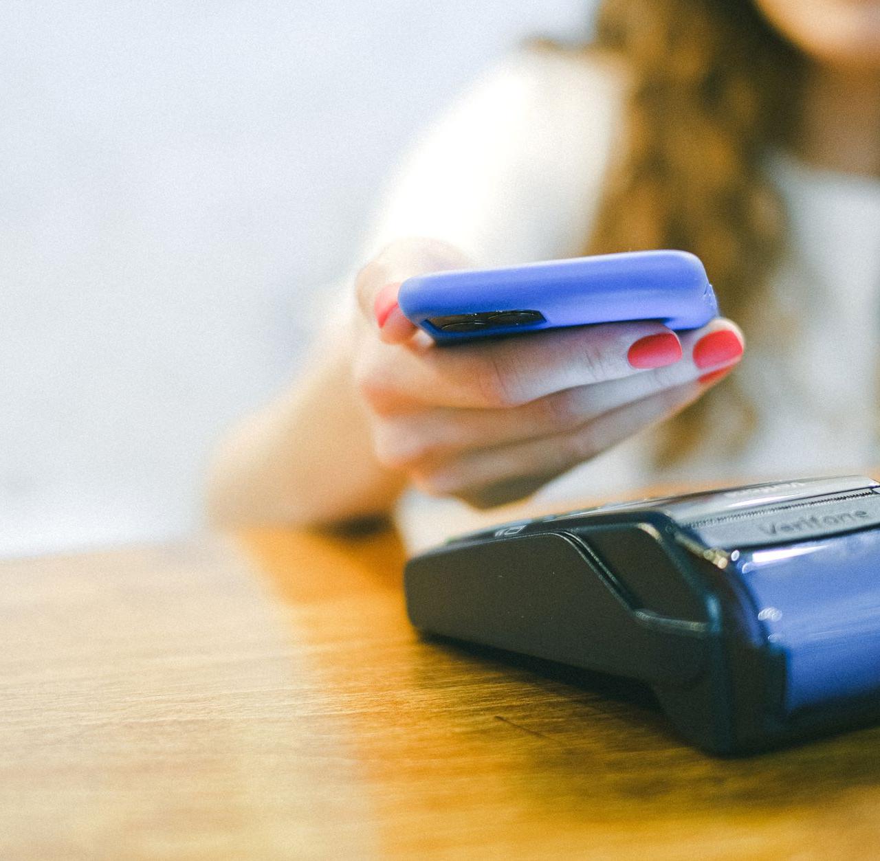 Close-up of a woman making a contactless payment using a smartphone over a card reader