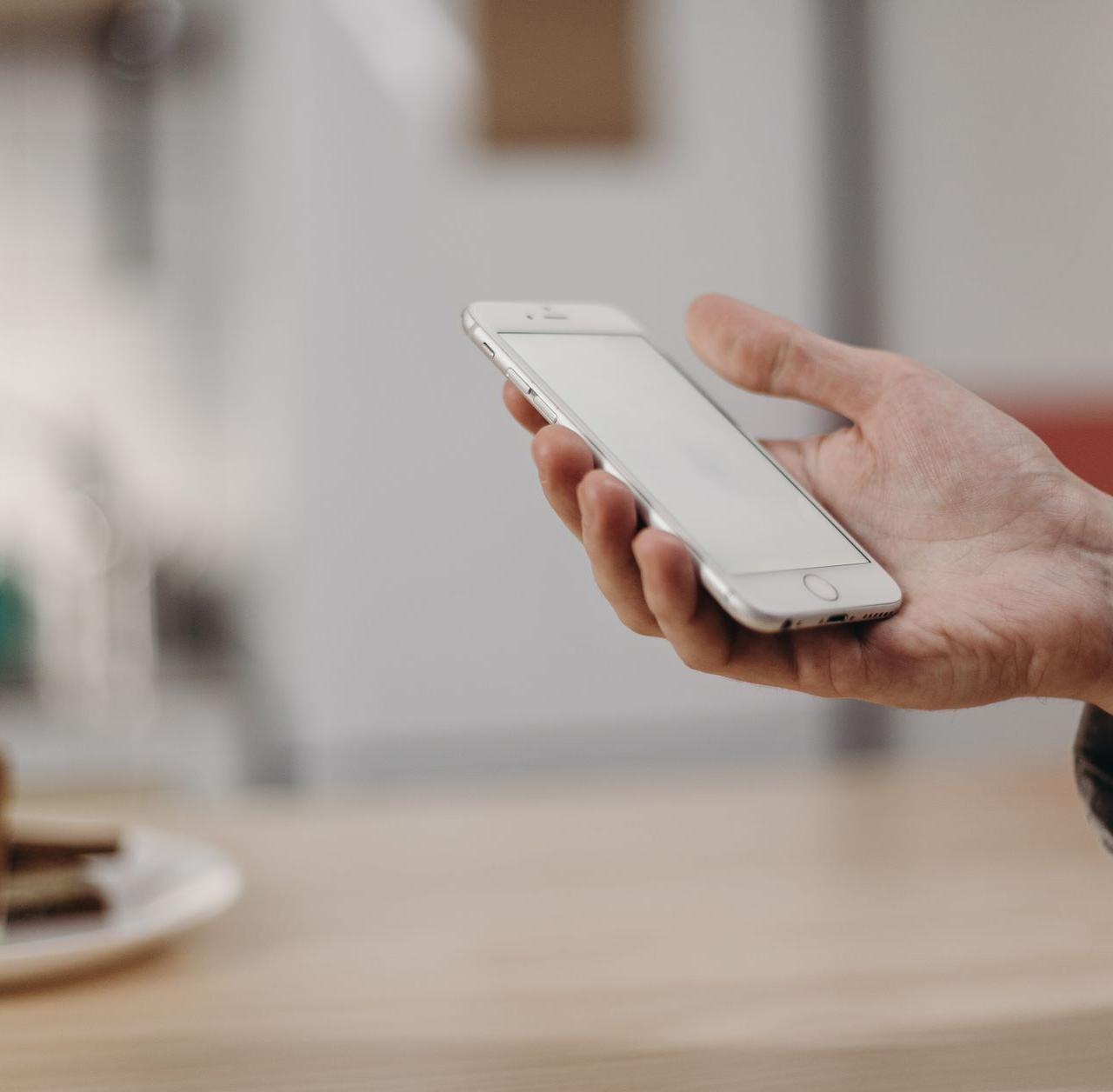 Person holding a smartphone in a cozy modern kitchen, showcasing technology in daily life.