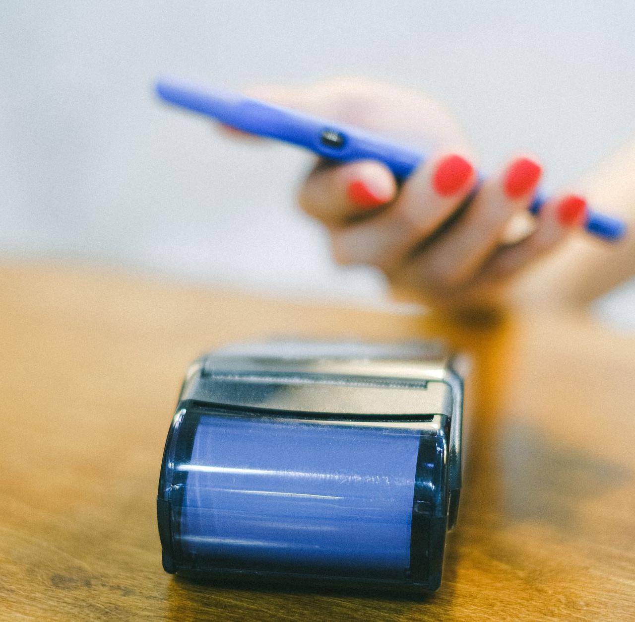Close-up of hand using smartphone for contactless payment at a terminal on wooden surface.