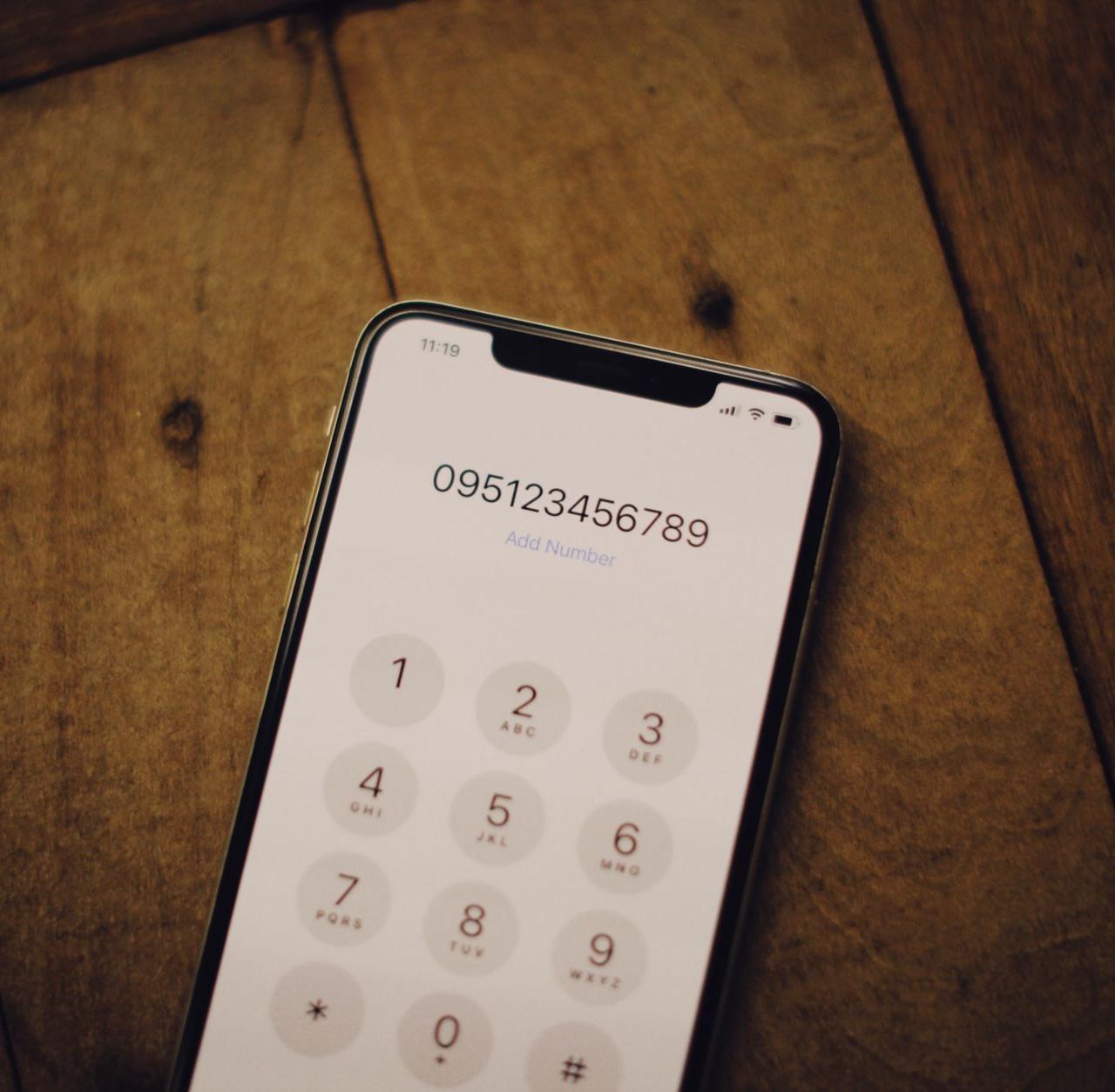 Close-up of a smartphone with a numeric dial pad placed on a wooden surface.