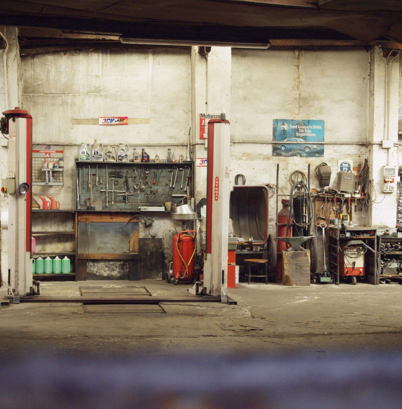 An empty, rustic car workshop featuring tools, machinery, and car lifts in an industrial setting.