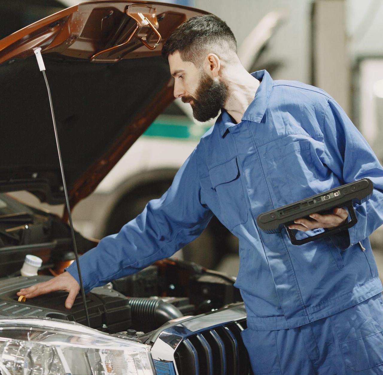 Professional mechanic examining a car engine under an open hood in a garage setting.