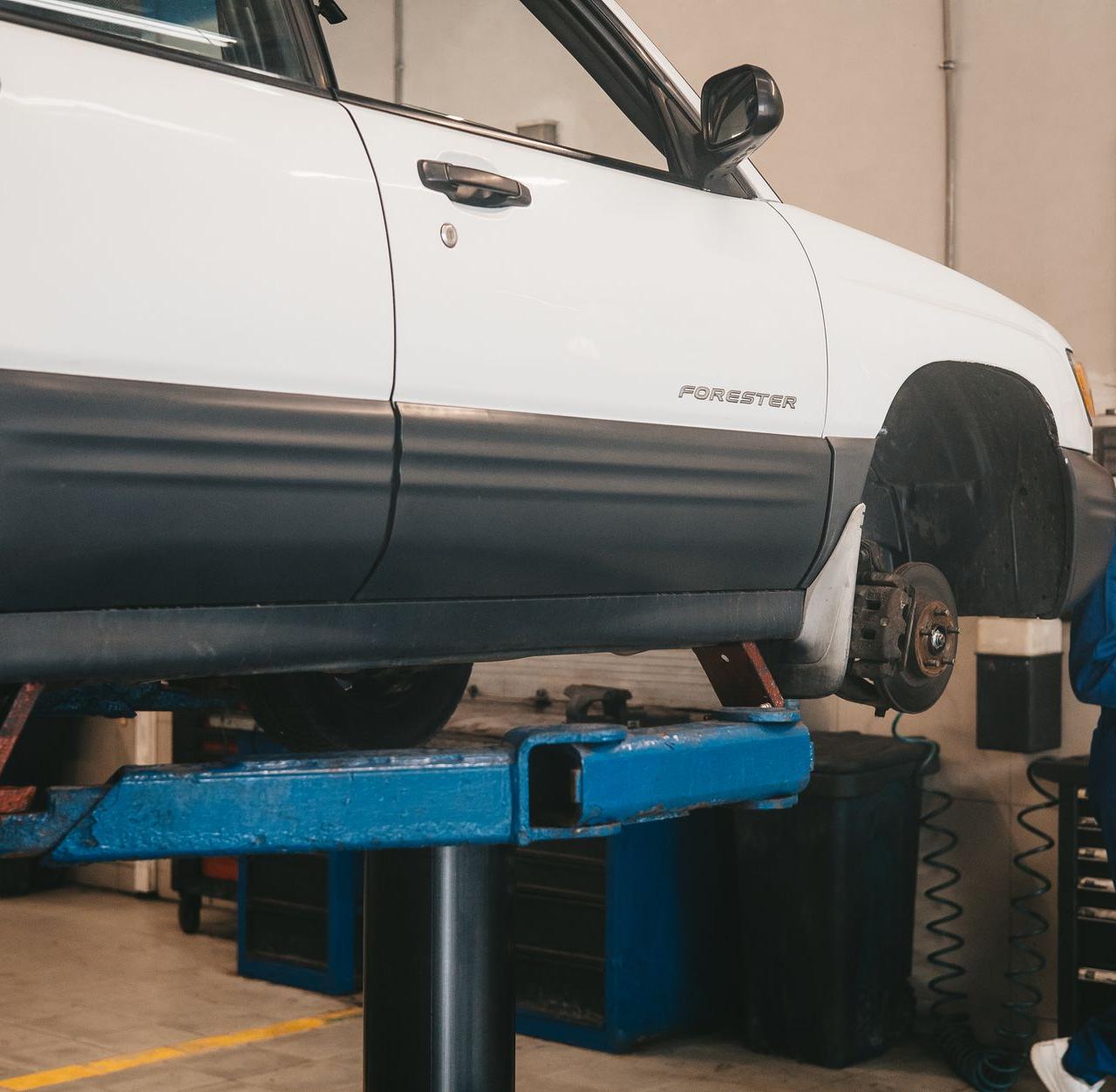 Mechanic evaluating a car on a lift for maintenance in an auto workshop.
