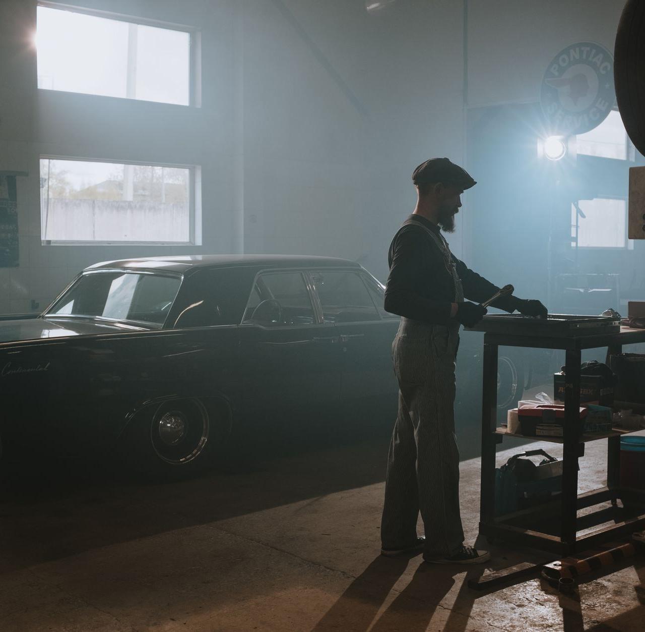 A mechanic working on a classic car in a dimly lit garage, showcasing vintage automotive repair.