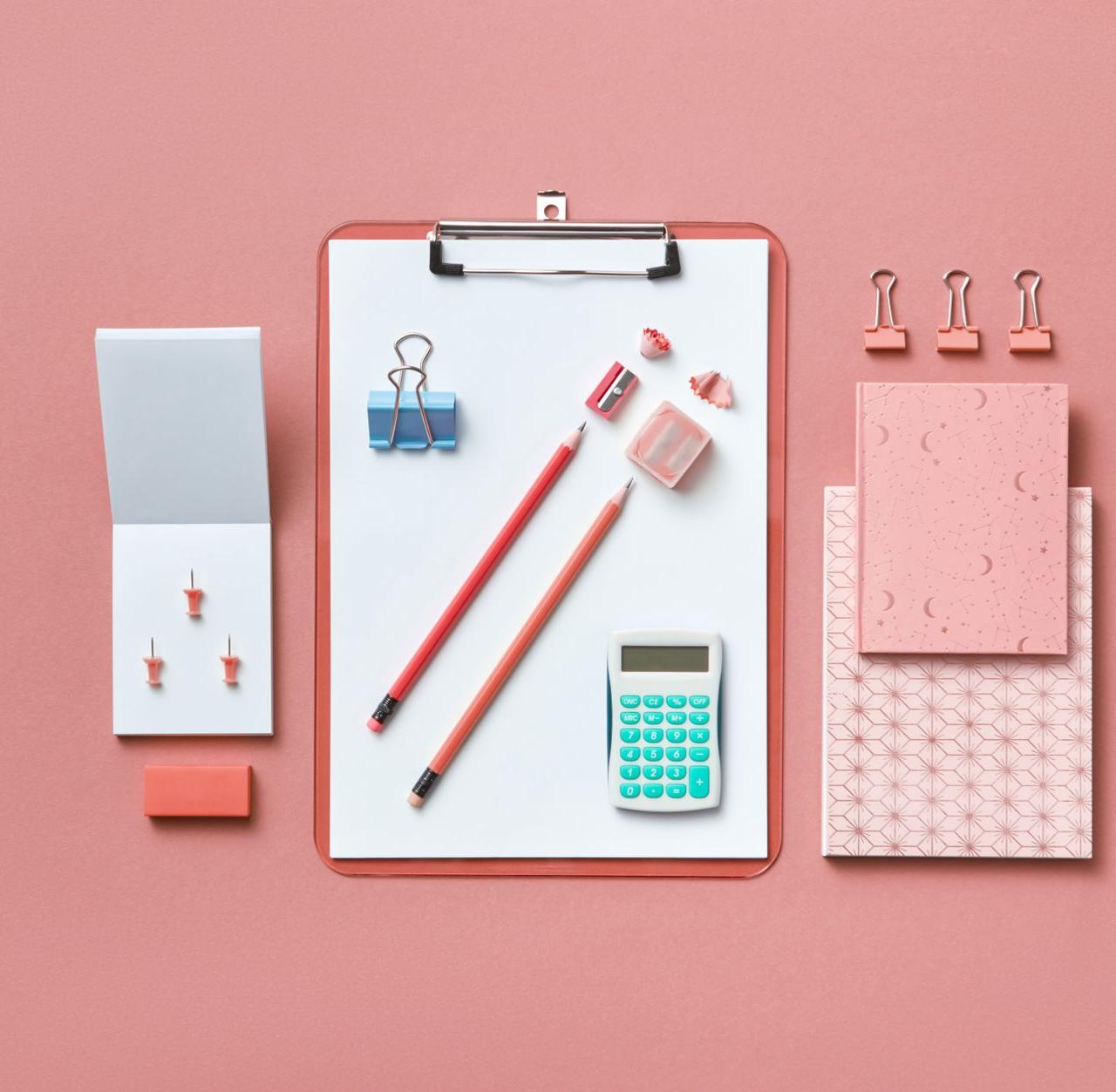 A modern flat lay of various office supplies arranged neatly on a pink background.