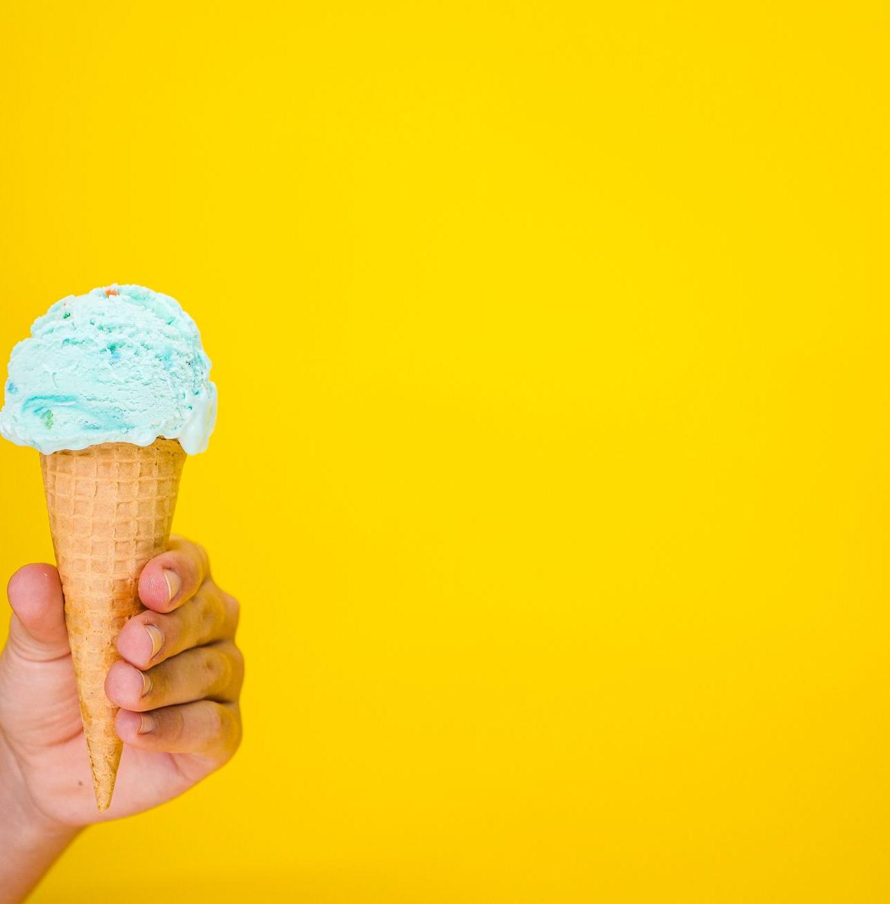 Close-up of a hand holding an ice cream cone with a vivid yellow backdrop.