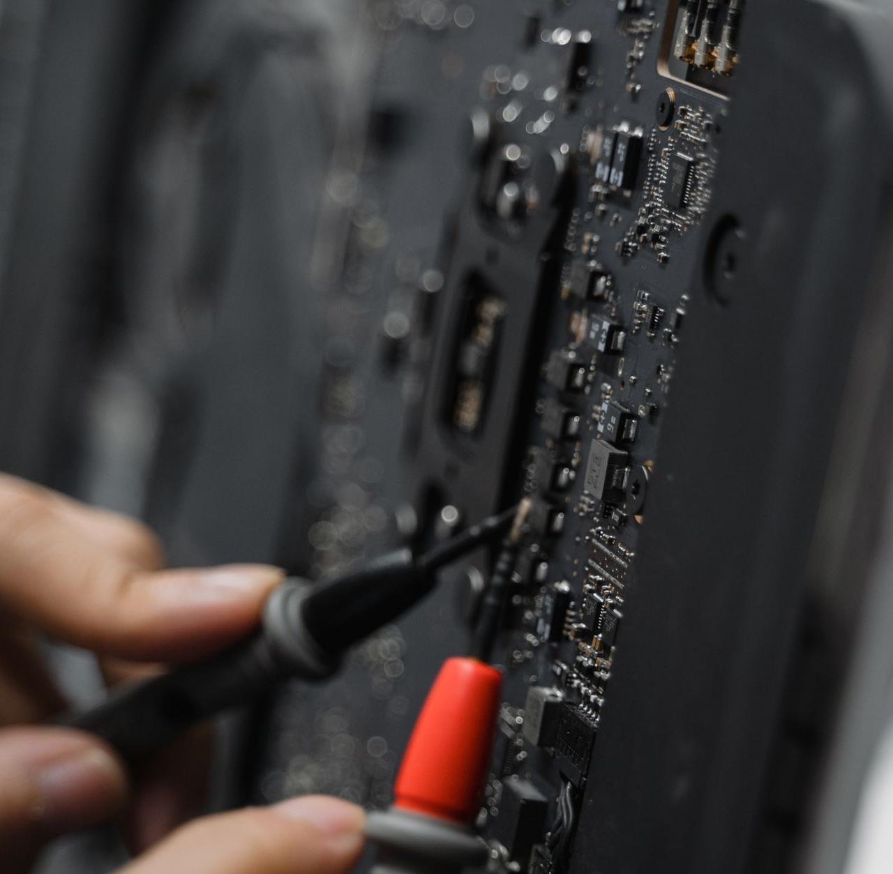 A technician uses tools to repair a circuit board, focusing on microelements.