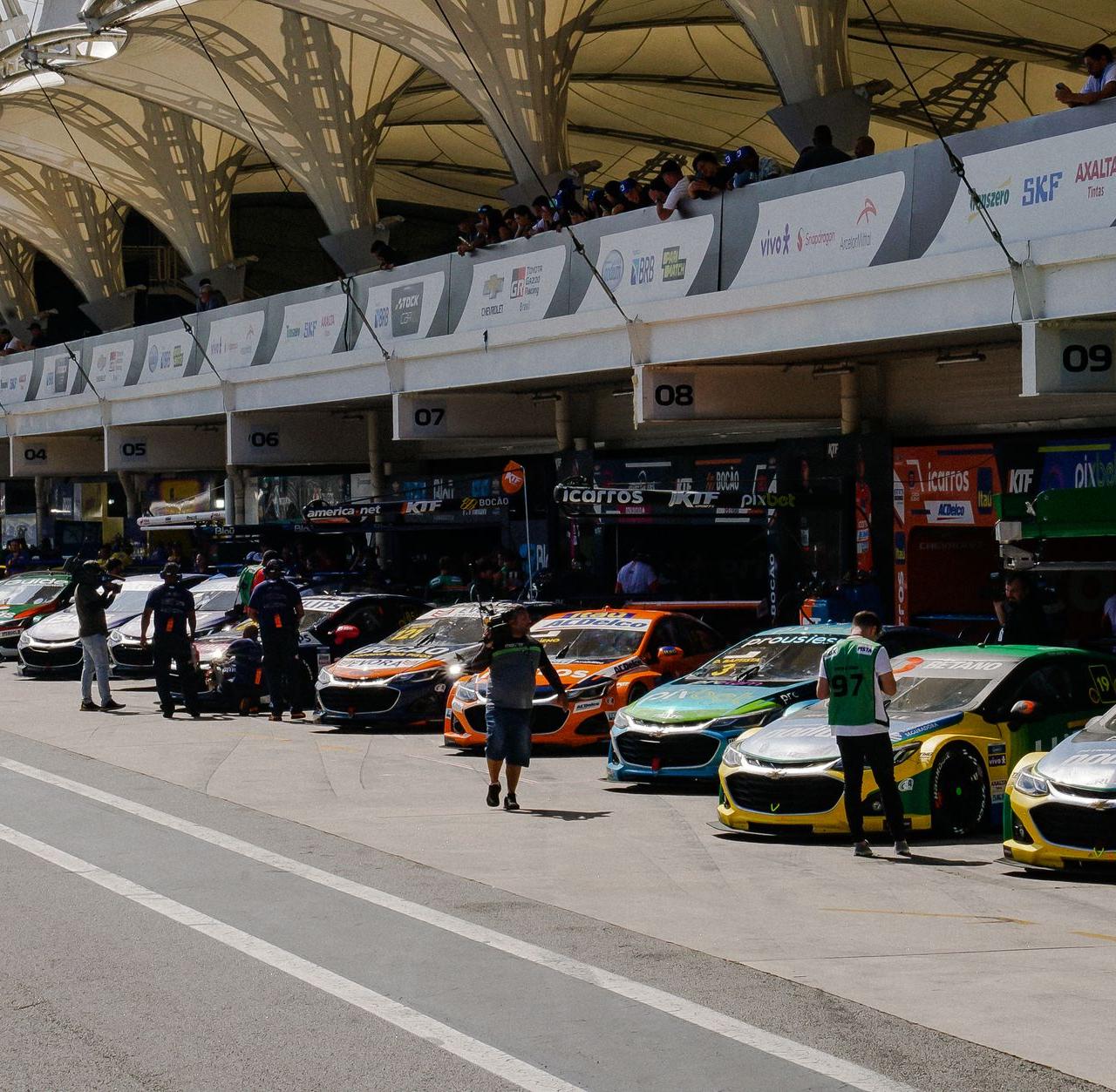 Stock cars lined up at the circuit garage during a sunny racing event.