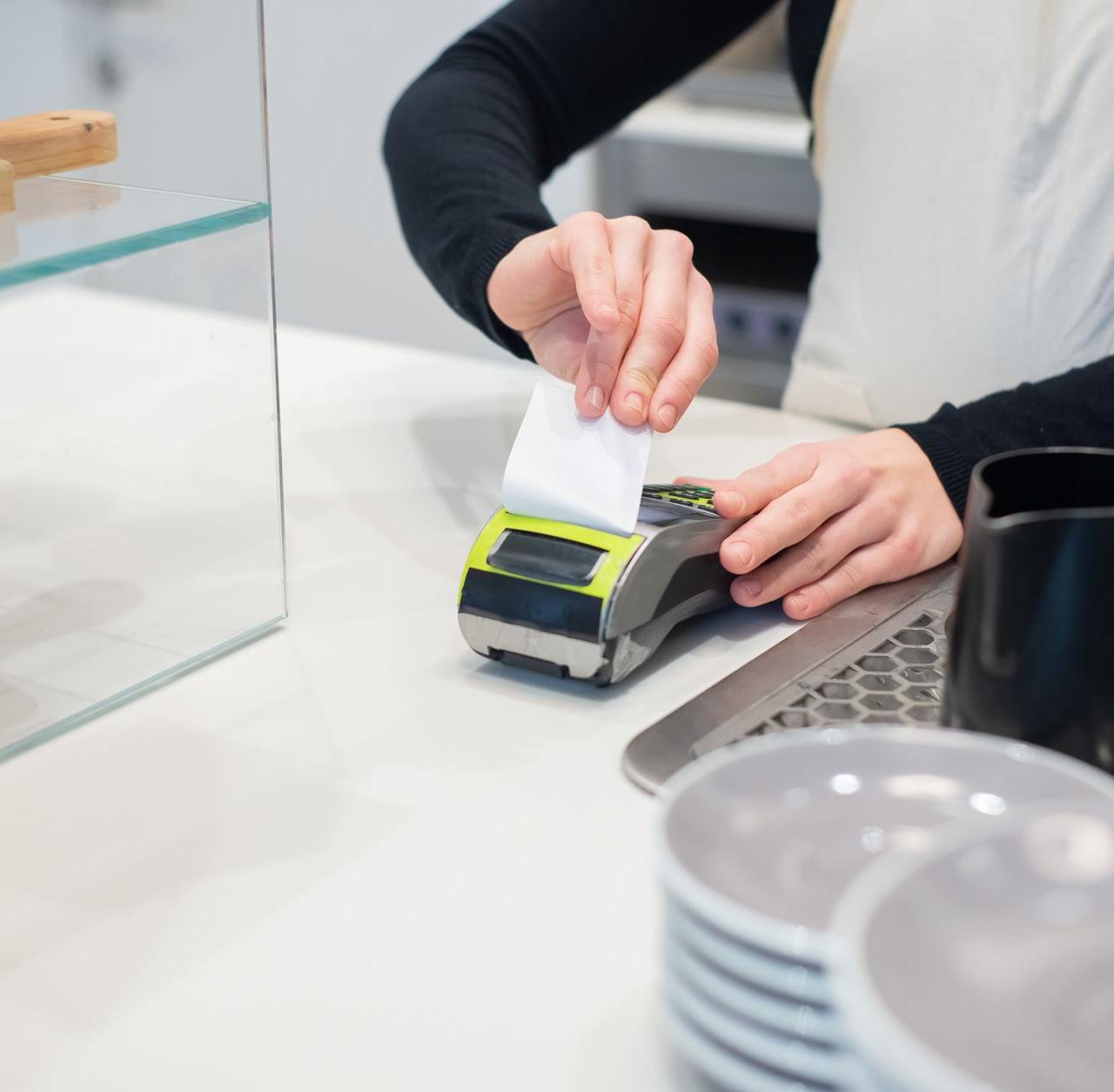 Close-up of a cashless transaction at a modern café counter with hands holding a receipt.