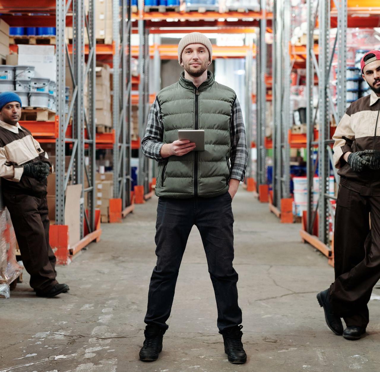 Three men in a warehouse standing among shelves with inventory.