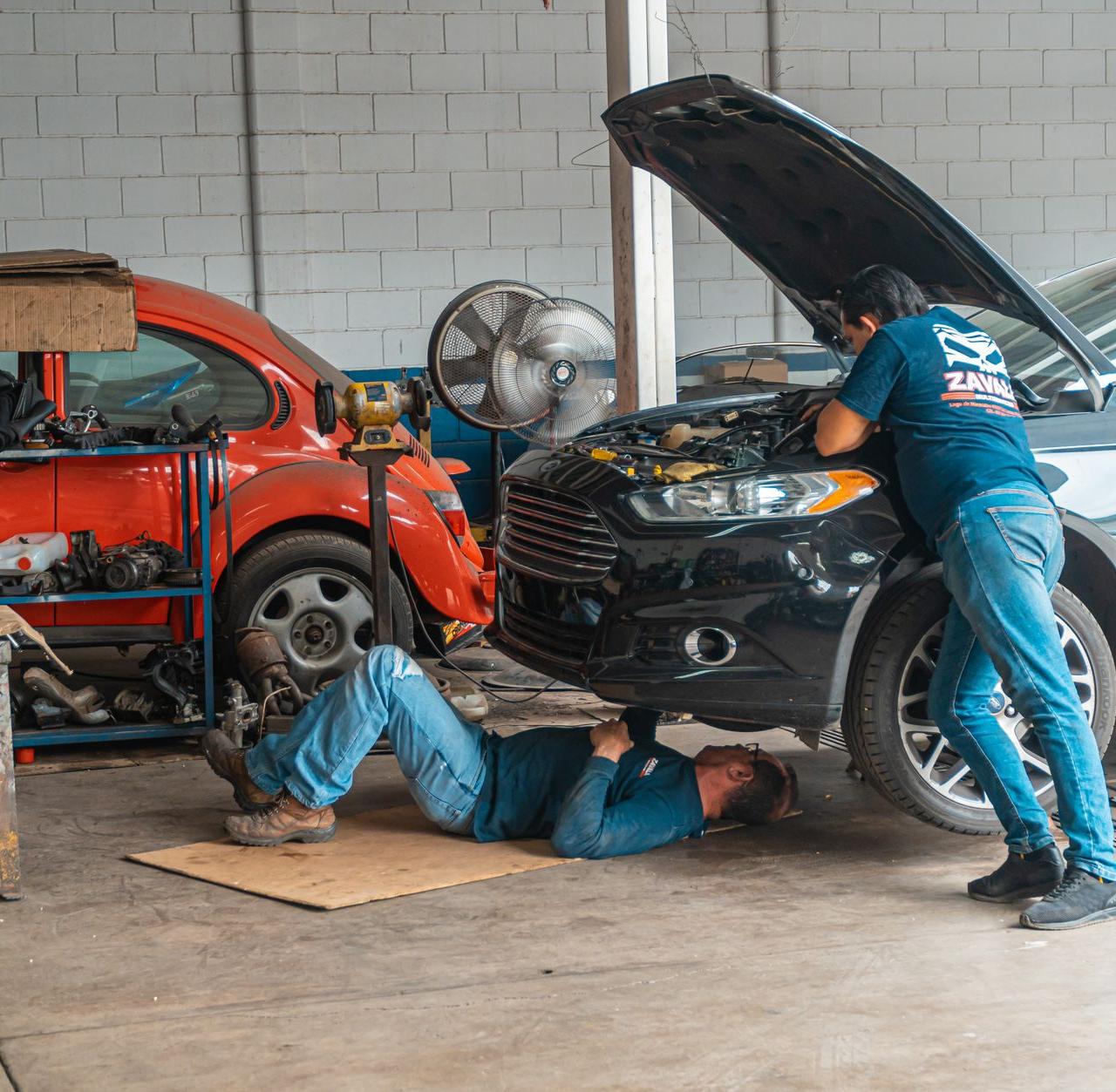 Mechanics working in an automotive workshop, repairing cars and performing maintenance.