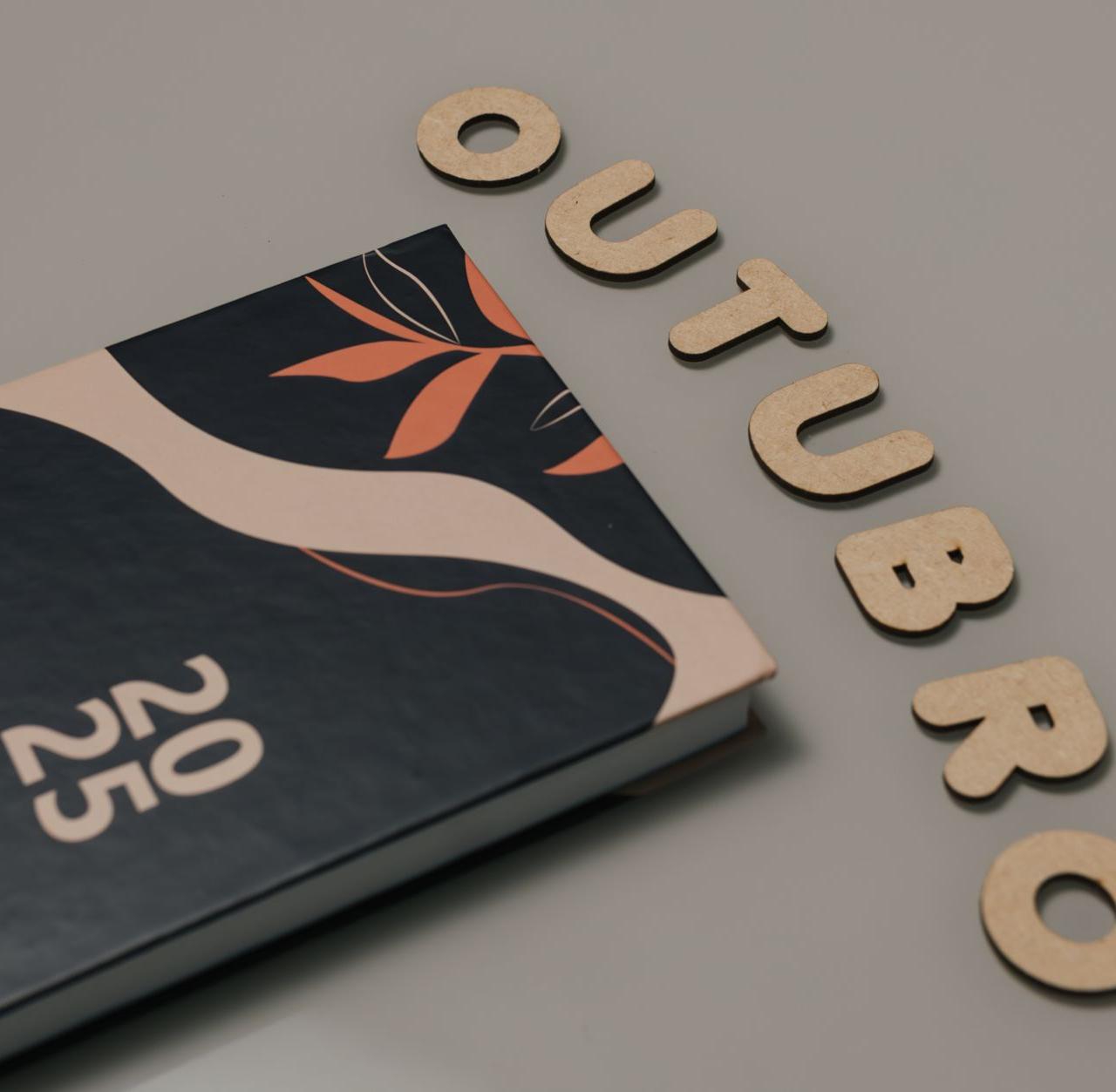 Minimalist flat lay featuring a 2025 planner and cut-out letters spelling 'OUTUBRO'.