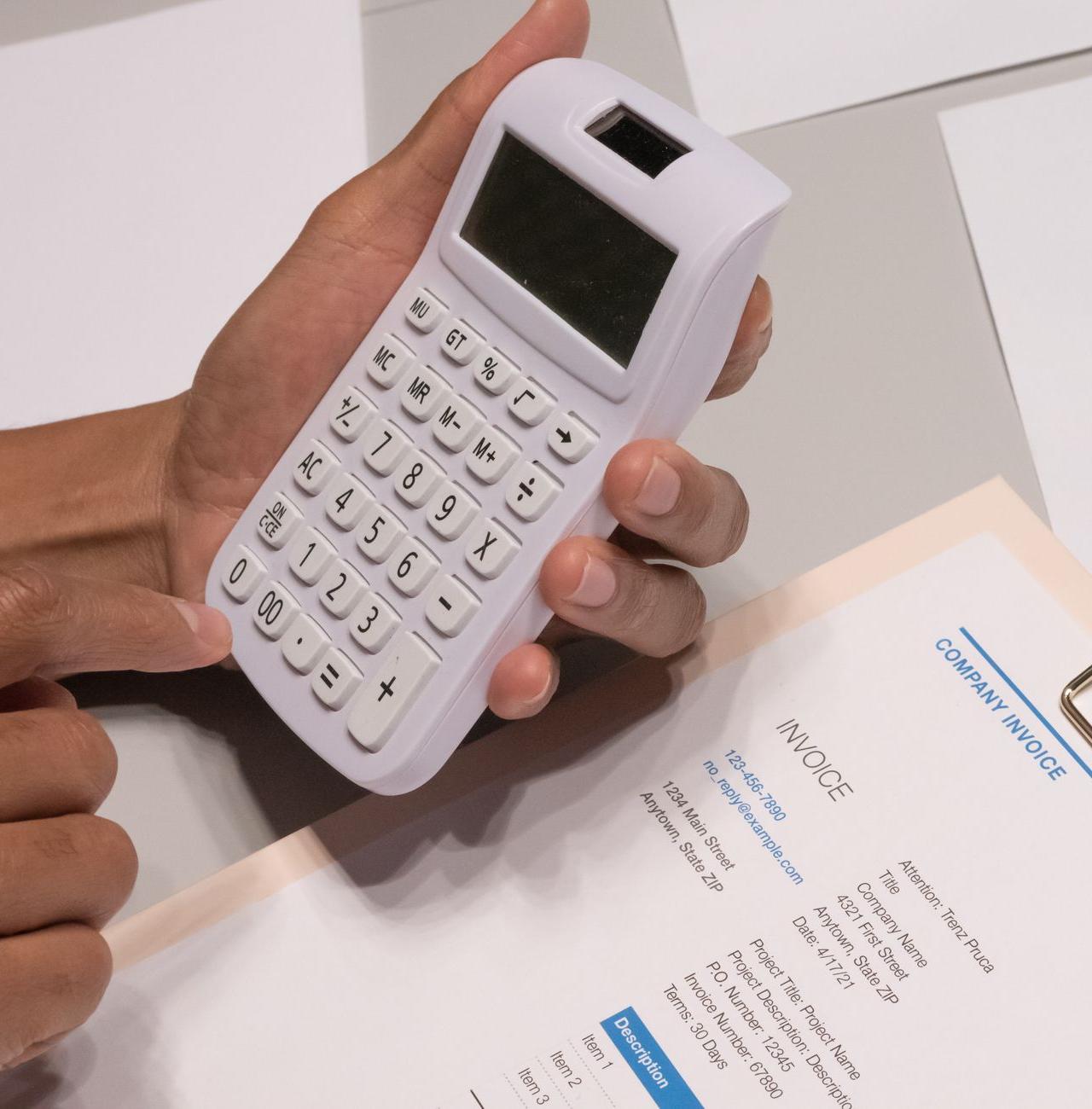 Close-up of hands using a calculator next to a company invoice, depicting a financial calculation concept.